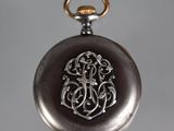 a silver pocket watch that has a monogram on it