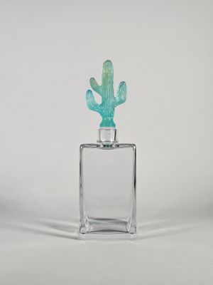 un petit cactus en verre posé sur un bloc de verre transparent