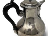 a silver teapot with a black handle on a white surface