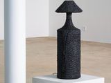une image représentant une sculpture noire posée sur un socle blanc dans une pièce