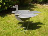 a metal sculpture of a bird on a stand in the grass