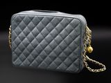 a grey quilted bag with a gold chain on a black background
