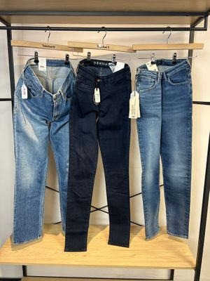 trois paires de jeans suspendues à un portant dans un magasin de vêtements