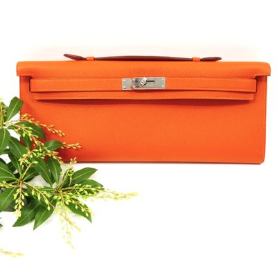 an orange purse sitting next to a plant on a white surface