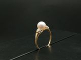 une image représentant une bague ornée d'une perle et de diamants posée sur un fond noir