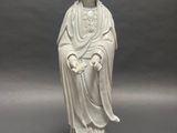 white statue of a woman sitting on a rock on a gray surface