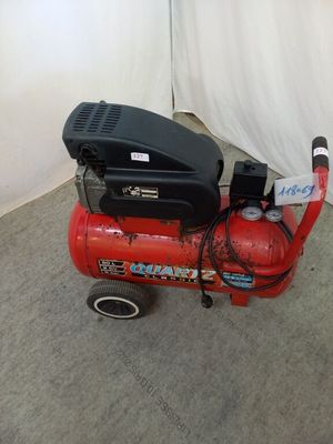 a red air compressor sitting on the floor next to a white curtain