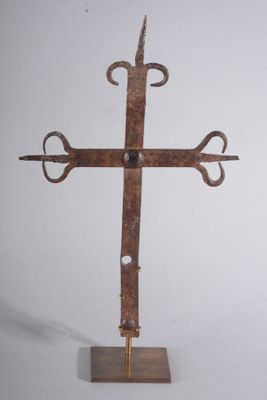 une croix en métal posée sur un socle en bois, sur fond blanc