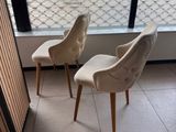 deux chaises beiges placées devant une fenêtre où se trouve un vase de fleurs