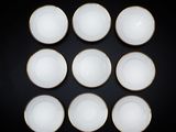 six bols blancs aux bords dorés posés sur un fond noir