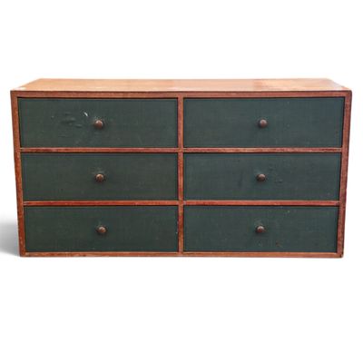 une image représentant une commode verte à quatre tiroirs, surmontée d'un plateau en bois
