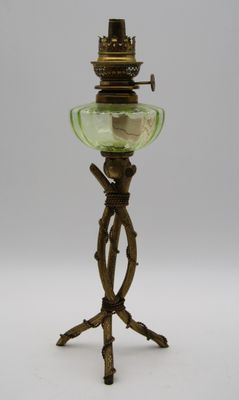 une lampe à huile ancienne en laiton et verre vert, posée sur un trépied