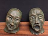 pair of bronze sculptures of two faces on a wooden surface