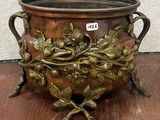 un grand pot en métal orné de fleurs, posé sur une table en bois