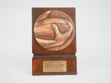 bronze plaque of a hand holding a soccer ball on a wooden base
