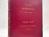 un livre rouge aux lettres dorées posé sur une surface blanche