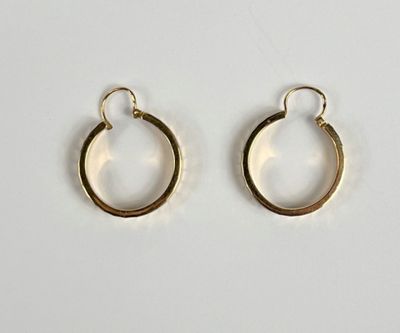 une paire de boucles d'oreilles créoles en or posées sur une surface blanche