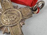 a silver cross on a red ribbon on a table