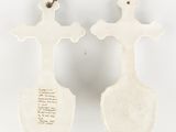 two white ceramic crosses with writing on them on a white surface