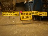 two signs that are on the ground near a dumpster