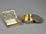two silver and gold plated boxes on a gray surface