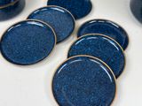 six blue plates sitting on a table with a vase in the background