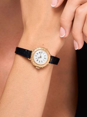 une femme portant à son poignet une montre en or au cadran blanc