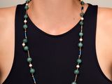 La femme porte un débardeur noir et un collier vert orné de perles.