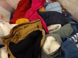 a pile of clothes on a bed with a teddy bear