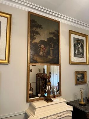 tableau accroché au mur au-dessus d'un miroir, dans une pièce où sont accrochées des photos aux murs