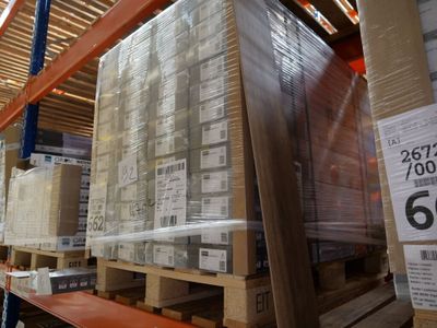 Les cartons sont empilés sur des palettes dans un entrepôt, et une étiquette de prix est apposée sur la palette.