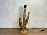 une lampe en forme de cactus dorée posée sur une table en bois, avec un cordon noir