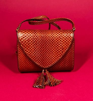 a brown snake skin purse with a tassel on a pink background