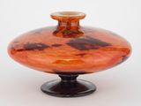 un vase orange avec un socle noir sur fond blanc