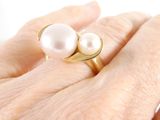 a woman ' s hand holding a ring with two pearls on it