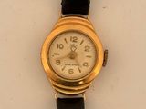 a gold watch on a black strap on a white surface
