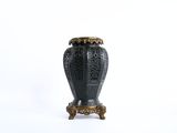 a black vase sitting on a stand on a white surface