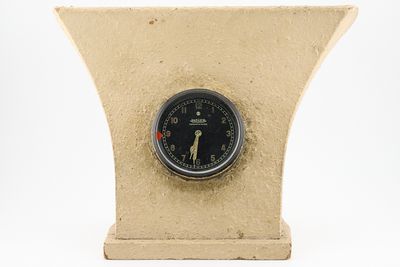 une horloge posée sur un support sur une surface blanche