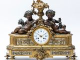 a gold clock with two cherensils on top of it