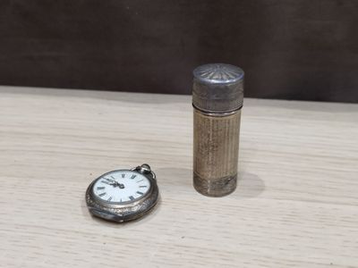 a small silver pocket watch next to a lighter on a table