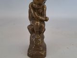 une petite statue en bronze représentant un garçon assis sur une souche d'arbre