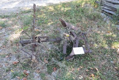 a rusty plow sitting in the grass next to a log