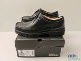 des chaussures de ville noires pour homme posées sur une boîte, sur une surface blanche