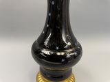 un vase noir avec un socle doré posé sur une table blanche