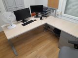 a desk with two monitors and a fan in the corner