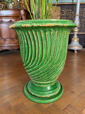 un vase vert contenant des fleurs, posé sur un parquet