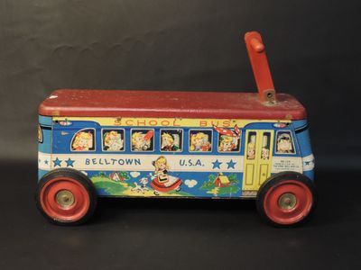 an old fashioned tin toy bus with a red handle on a black surface