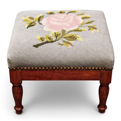 an upholstered foot stool with a needled rose on it