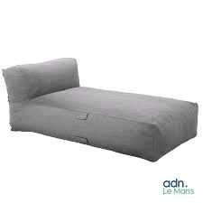une chaise longue en forme de pouf grise, sur laquelle est posé un coussin