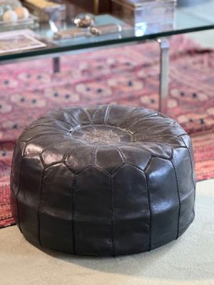 a black leather pouffe sitting on the floor in a living room